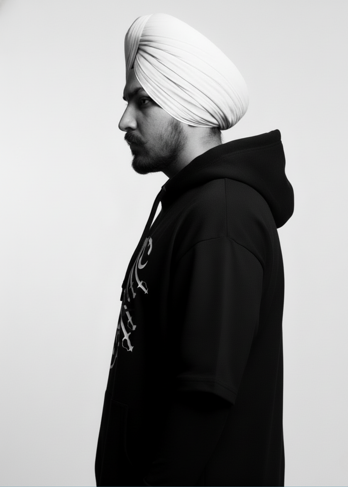 Sikh turbaned male wearing a black Cotton Fleece Hoodie with a white graphic design featuring panjabi Shastar with "Stay Fearless" written in red on a plain background.