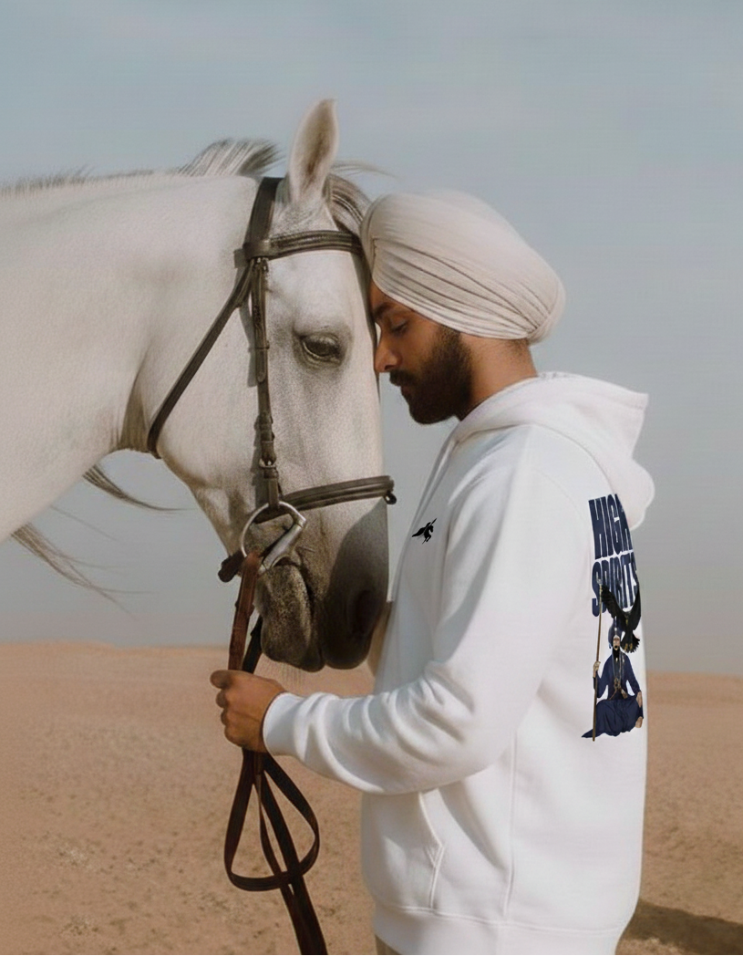 A man wearing a white turban and a white hoodie with a "HIGH SPIRITS" graphic on the back is shown in profile, with his head gently touching the head of a white horse. He is holding the horse's reins. The setting appears to be a desert or sandy landscape under a pale sky. The image conveys a sense of calm and connection between the man and the horse.