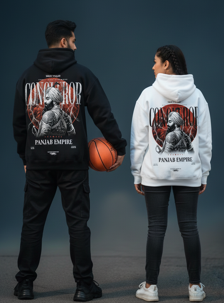 A male and female model stand with their backs to the viewer, each wearing a hoodie featuring a "CONQUEROR PANJAB EMPIRE" graphic with a central figure. The male model on the left wears a black hoodie, black cargo pants, and holds a basketball under his arm, looking to his right. The female model on the right wears a white hoodie and dark jeans, looking to her left. They are positioned against a dark blue-grey background.