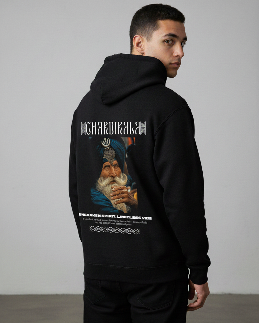 Person wearing a black hoodie with a graphic design of a Sikh elderly man wearing a navy blue turban and t-shirt with a khanda on the turban staring depicted on the back with "Chardikala" written on the top, "Limitless vibe, Unlimited Spirit" on the bottom against a gray background